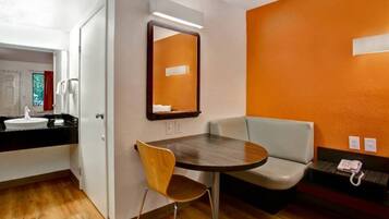 A hotel room with a round table, a chair, a sofa, a mirror, and a telephone.