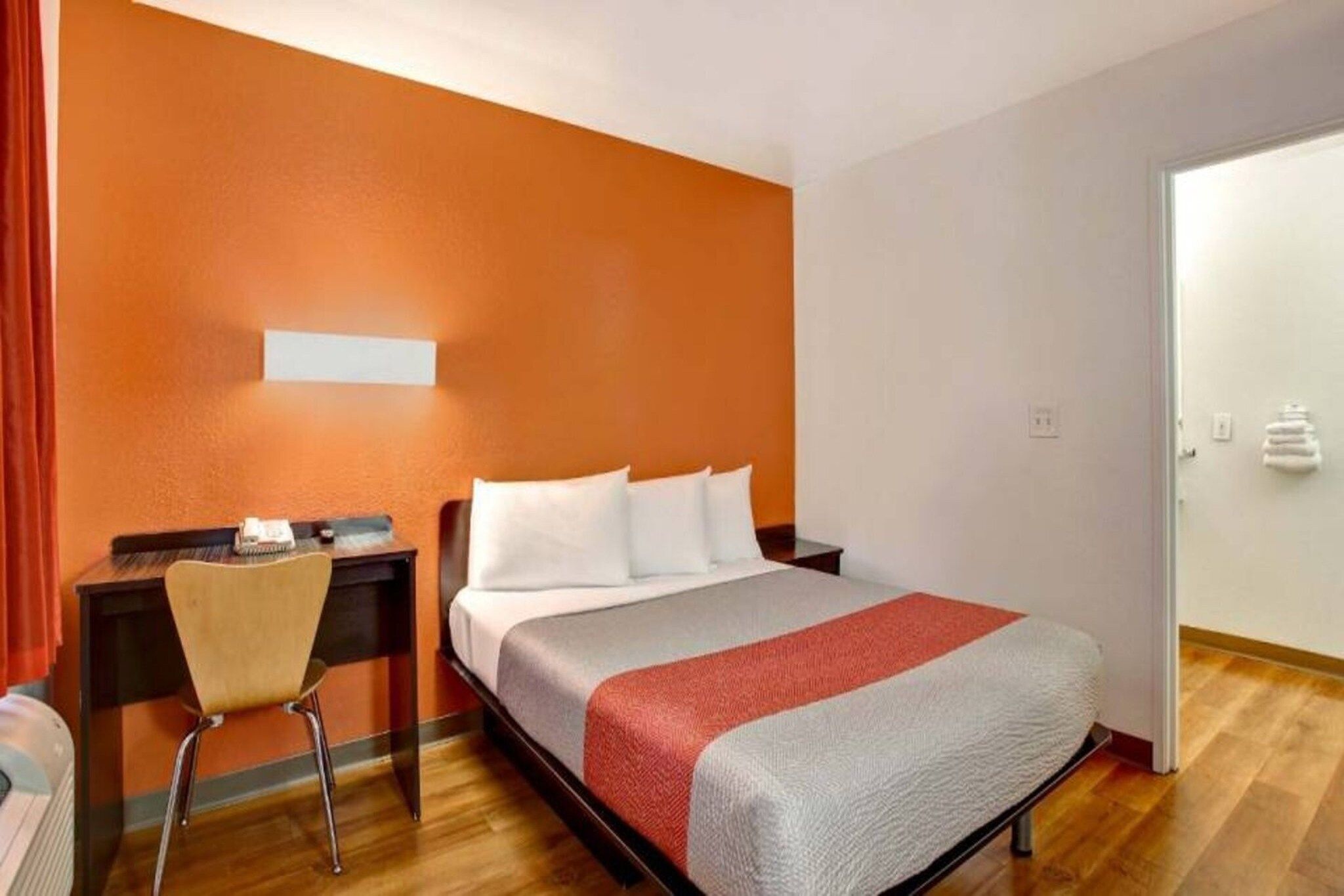 A hotel room with a bed, a desk, a chair, and a door.