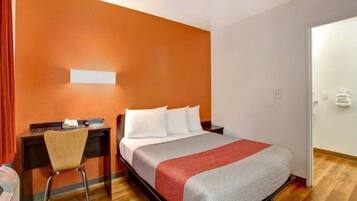 A hotel room with a bed, a desk, a chair, and a door.