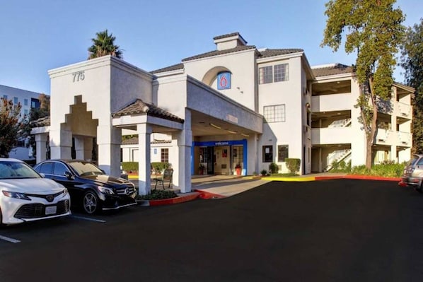 Un hotel con una facciata moderna, un ingresso ben visibile e un parcheggio con diverse auto.