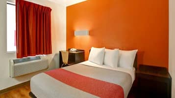 A hotel room with a bed, a bedside table, a heater, and a window with curtains.