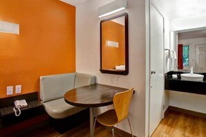 Una camera d'albergo con un tavolino rotondo, un divano, uno specchio e un bagno con un lavandino e specchio.