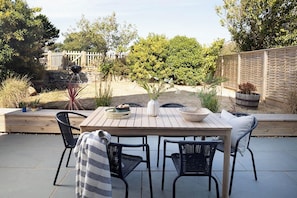 An outdoor patio with a wooden table and black chairs, surrounded by potted plants and a wooden fence. - Wood Cottage (Wadebridge)