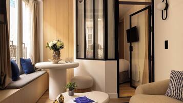 Une chambre d’hôtel moderne avec un canapé, une petite table sur laquelle est posé un livre, un vase avec des fleurs et une vue sur la ville par la fenêtre.