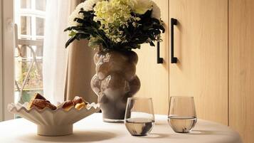 A round table with a white vase of flowers, two glasses, and a plate of food.