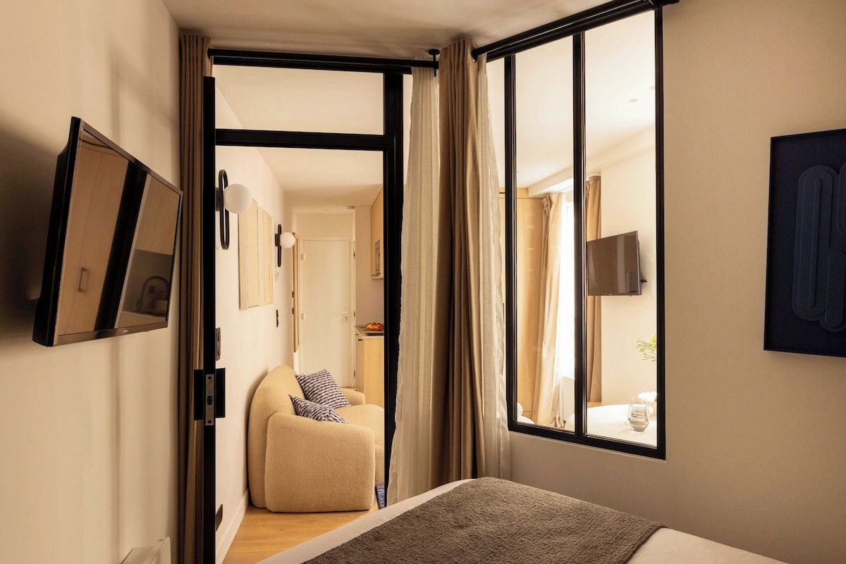 Une chambre d’hôtel avec un lit, un canapé, une télévision et une grande fenêtre avec des rideaux.