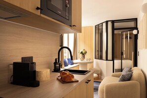 Een compacte keuken met een inbouw-Bosch magnetron, een klein spoelgedeelte en een zithoek met een bank en een fauteuil.