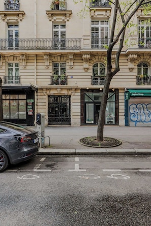 A street view with a parked car, a sidewalk, a tree, and a building with a storefront. - A Real Paris Experience : Walk to Montmartre ! (Paris)