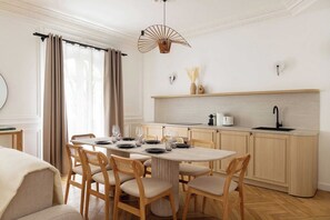 A dining area with a round table, wooden chairs, and a kitchen in the background. - A Real Paris Experience : Walk to Montmartre ! (Paris)