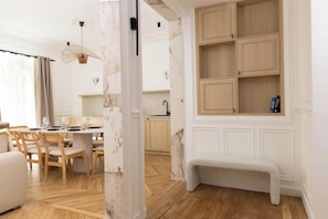 A room with a dining area, a bench, and a kitchen with wooden cabinets. - A Real Paris Experience : Walk to Montmartre ! (Paris)