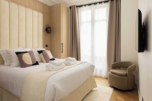 Een hotelkamer met een groot bed, een fauteuil, een flatscreen televisie en een raam met gordijnen.