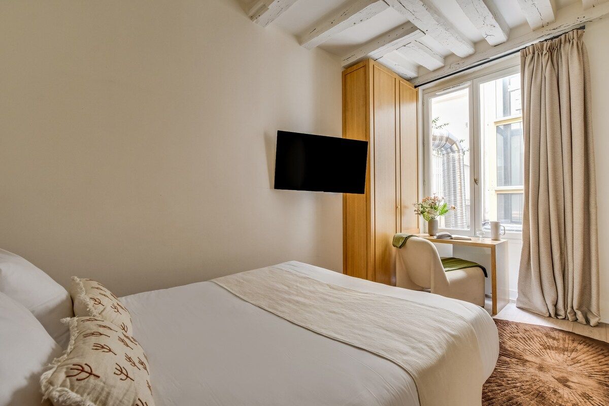 Een hotelkamer met een bed, een bureau met stoel, een televisie en een raam met gordijnen.