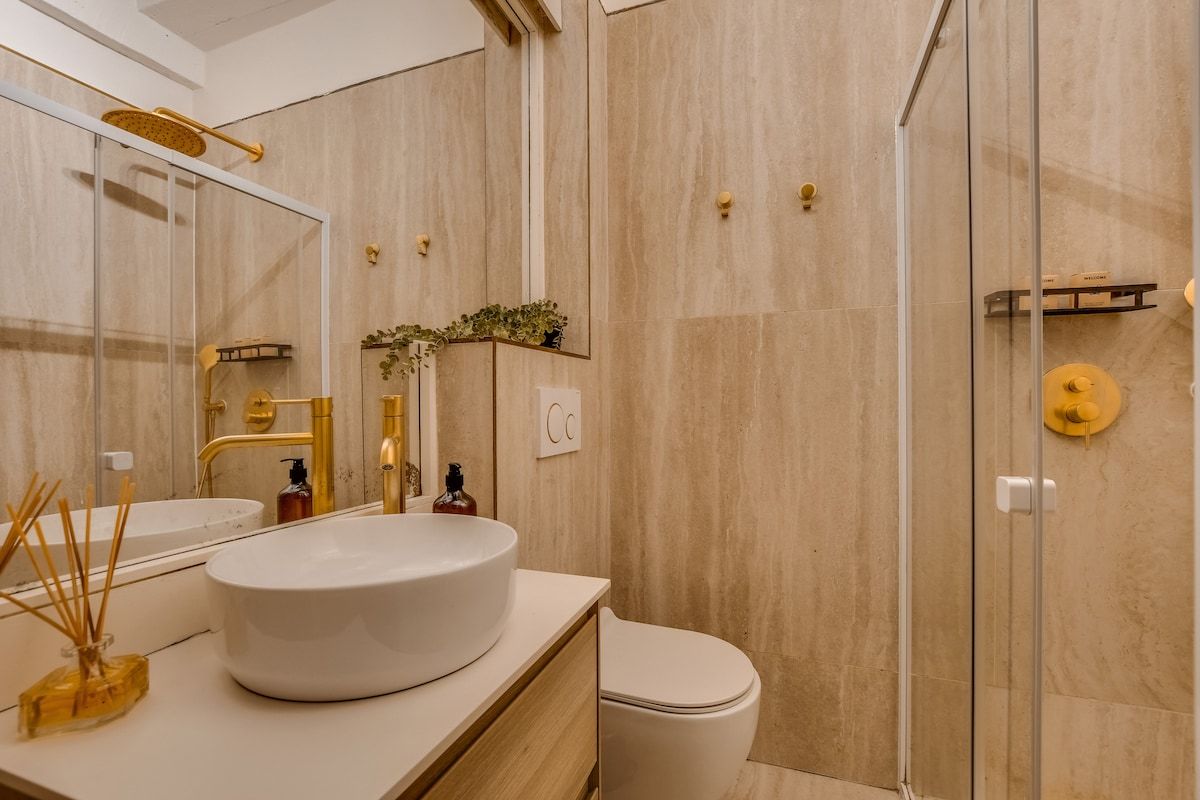 A modern bathroom with a large mirror, a round sink, a toilet, and a glass shower enclosure.