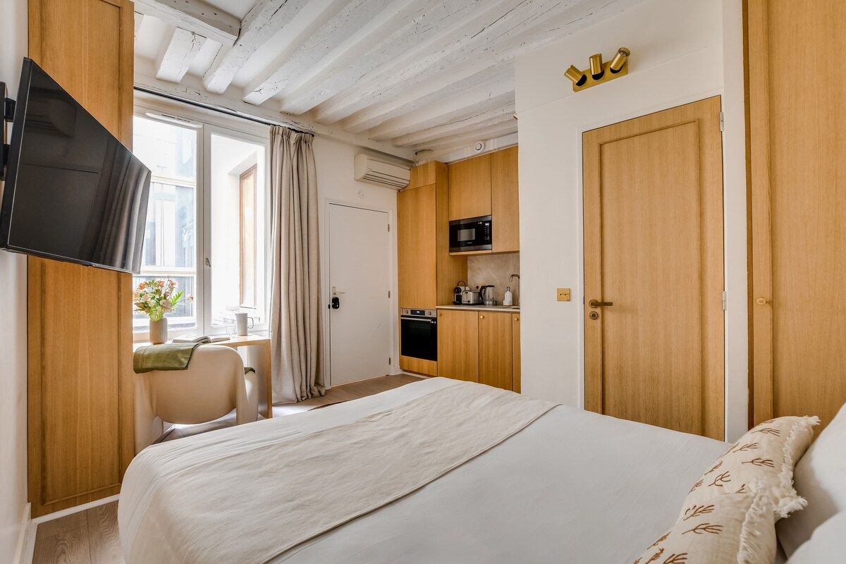 Una camera d'albergo con un letto, una scrivania con una sedia, una televisione, angolo cottura e una porta.