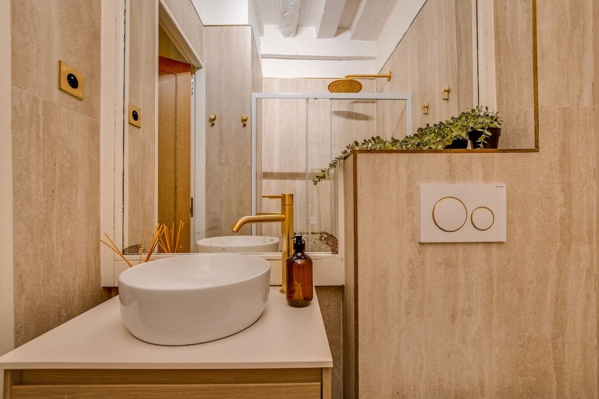 Une salle de bain moderne avec un lavabo rond, des accessoires dorés et un miroir.