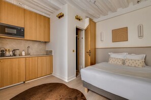 Een compacte hotelkamer met een kitchenette, een bed met witte beddengoed en een houten vloer.