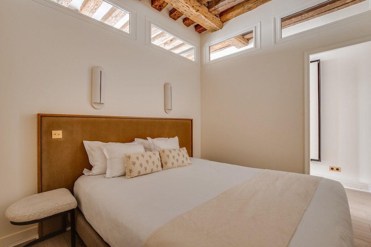 A bedroom with a large bed, a bench, and skylights.