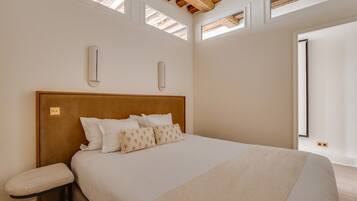 A bedroom with a large bed, a bench, and skylights.