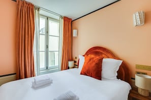 A hotel room with a large bed, orange curtains, a window with a view, and a bedside lamp. - Live Like a Real Parisian in the Centre of Paris (Paris)