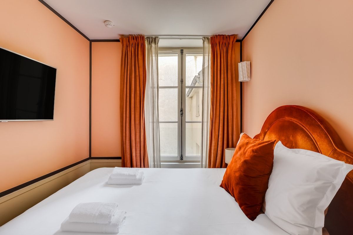 A hotel room with a bed, a flat-screen TV mounted on the wall, and a window with curtains.