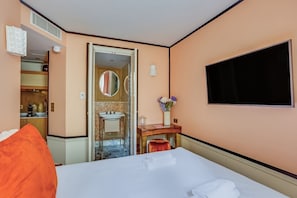 Ein Hotelzimmer mit Bett, Schreibtisch, Spiegel, Fernseher und einem durchgegangenen Tür sichtbar liegenden Badezimmer.