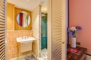 Ein Badezimmer mit einem weißen Waschbecken, einem runden Spiegel, einer Dusche mit goldener Duschbrause und einer Vase mit Blumen auf der Ablagefläche.