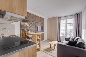 Une cuisine moderne dotée d’une cuisinière intégrée, un coin repas avec une table et des chaises en bois, et un salon avec un canapé et un téléviseur.