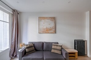 A modern living room with a grey sofa, a wall-mounted abstract painting, and a radiator. - Peaceful Studio for a Calm & Soothing Retreat (Paris)