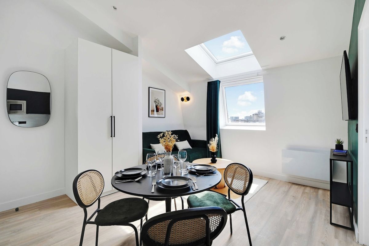 Un espace de repas moderne avec une table ronde pour quatre personnes, un canapé, un téléviseur et une lucarne au-dessus.