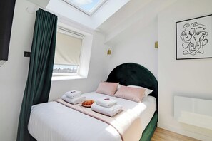 A bedroom with a skylight, a bed with pillows and towels, a wall art piece, and a window with curtains. - Breathtaking View over Parisian Skyline - Voltaire (Paris)