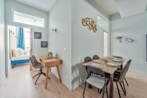 A dining area with a wooden table set for four, a sofa, and a staircase leading to an upper level. - Spacious & Modern Apartment - Central Le Marais (Paris)