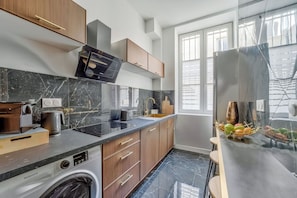 A modern kitchen with a built-in washing machine, a large window, and a stainless steel refrigerator. - Spacious & Modern Apartment - Central Le Marais (Paris)