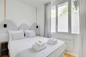 A bedroom with a bed, pillows, a nightstand, a window, and a view of the outside. - Your Parisian Home Base in the 18th District (Paris)