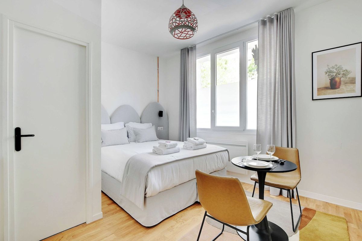 A hotel room with a bed, a round table with chairs, a door, and a window with curtains.