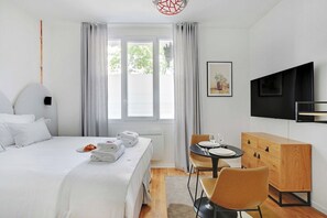Quarto de hotel com cama, mesa de jantar com cadeiras, televisão e um armário de madeira.