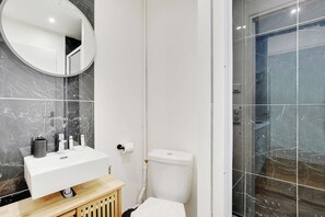 A bathroom with a white sink, mirror, toilet, and shower. - Your Parisian Home Base in the 18th District (Paris)