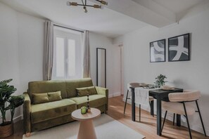 A living room with a sofa, a dining table, chairs, a small round table, and a potted plant. - Clean & Modern Flat near Vibrant Bastille (Paris)