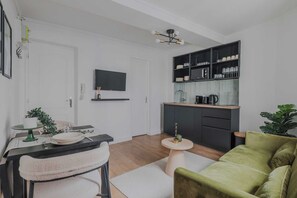 Un salon moderne comprenant un canapé, une table à manger avec des chaises, un coin cuisine avec des placards et un téléviseur.