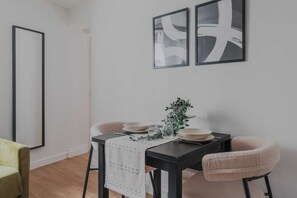 Un coin repas avec une table dressée pour deux personnes, un vase agrémenté de verdure et des œuvres d’art abstraites accrochées au mur.