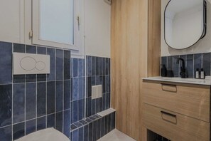 A bathroom with dark blue tiles, a wooden cabinet, a white countertop, and a mirror. - Clean & Modern Flat near Vibrant Bastille (Paris)