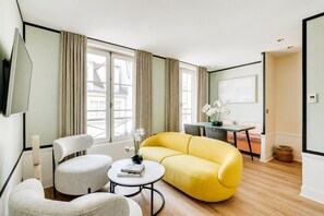 A modern living room with a yellow sofa, two armchairs, a coffee table, and a dining area with a table and chairs. - Stylish Duplex in the Heart of Le Marais (Paris)