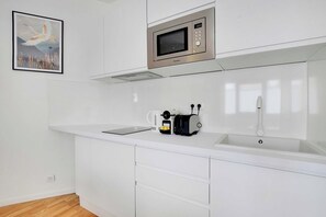A modern kitchen with white cabinetry, a stainless steel microwave, a coffee maker, and a sink. - Comfortable Cocoon to explore Paris (Paris)