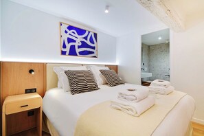 A modern hotel room with a large bed, a bedside table, a wall-mounted artwork, and a bathroom visible through an open door. - Stunning Flat in the Absolute Centre of Paris (Paris)