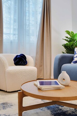 A living room with a round wooden coffee table, a beige armchair, a blue sofa, and a potted plant. - Stunning Flat in the Absolute Centre of Paris (Paris)