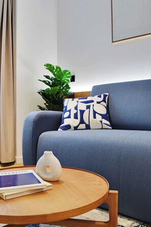 A modern living room with a blue sofa, a decorative pillow, a small vase, and a book on a round wooden table. - Stunning Flat in the Absolute Centre of Paris (Paris)