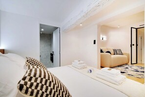 A modern hotel room with a large bed, a sofa, and a bathroom visible through an open door. - Stunning Flat in the Absolute Centre of Paris (Paris)