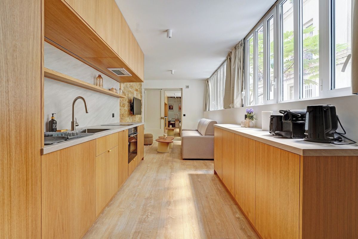 A modern kitchen with wooden cabinets, a built-in oven, and a large window providing natural light.