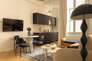 Ein modernes Wohnzimmer mit Essbereich, einer Küche mit dunklen Schränken, einem an der Wand montierten Flachbildfernseher und einer großen Stehlampe.