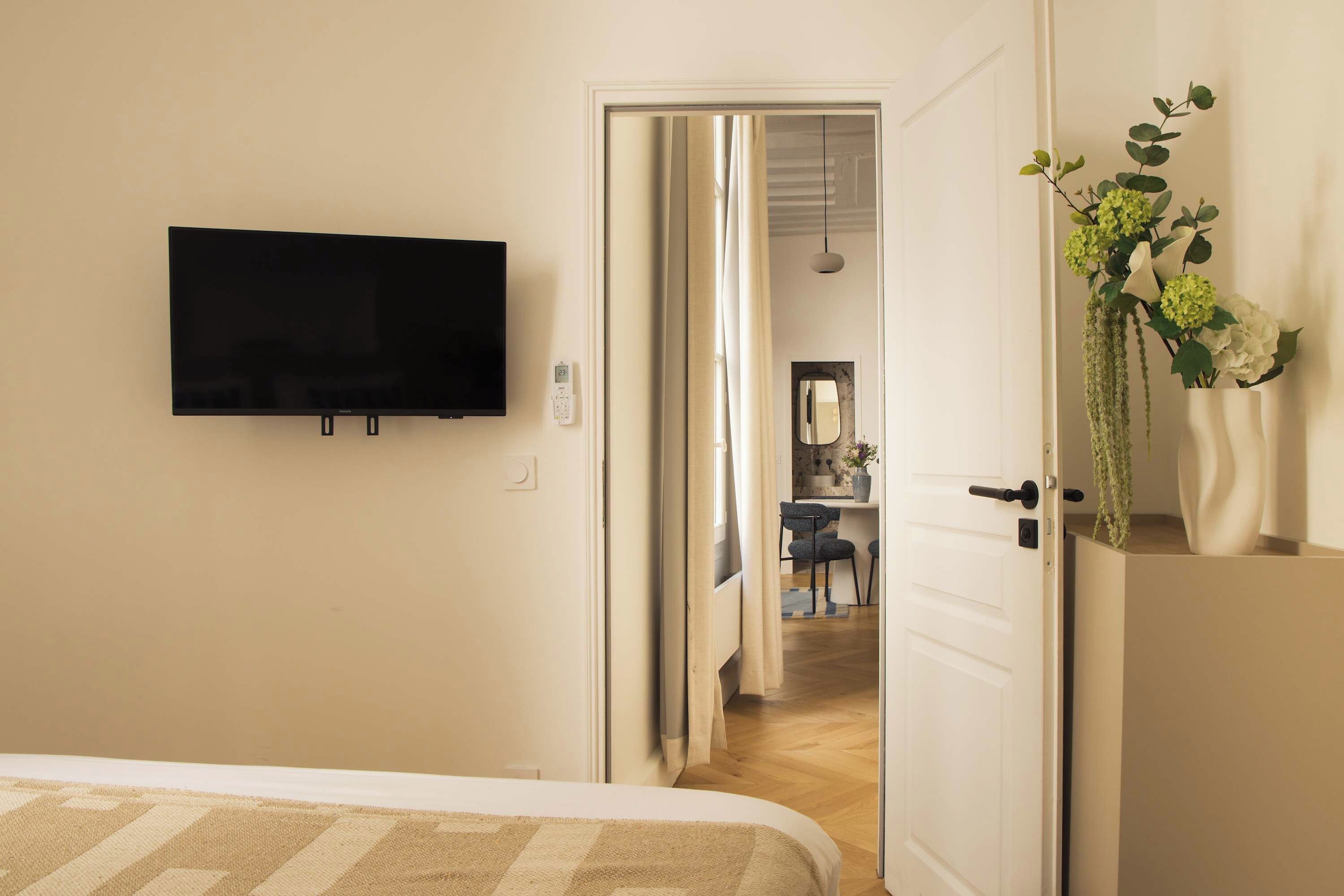 Une chambre d’hôtel comprenant un lit, un téléviseur fixé au mur, une porte donnant accès à une salle de bain et un petit bureau avec une chaise.