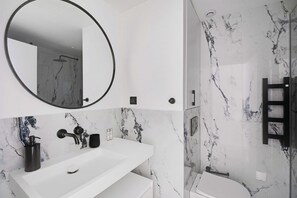 A modern bathroom with a white sink, a round mirror, and a shower area. - Chic Hideaway in Heart of Paris (Paris)